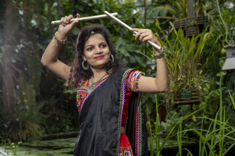 A woman in traditional Indian attire holding a gardening tool in a lush green botanical garden.