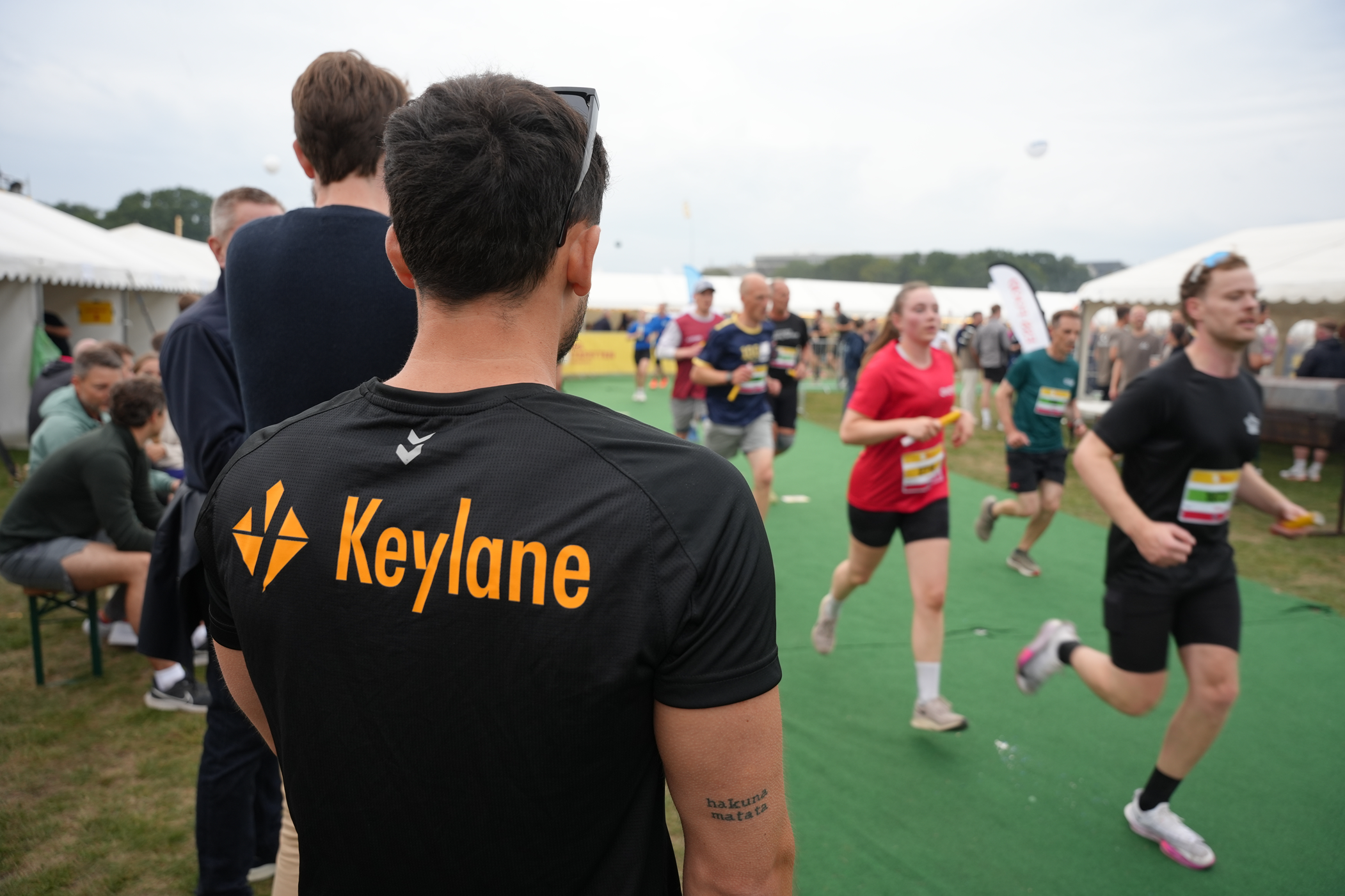 Diversity of people participating in a running event, with a focus on a person wearing a Keylane-branded shirt, emphasizing careers, professional growth, and active workplace culture at Keylane.